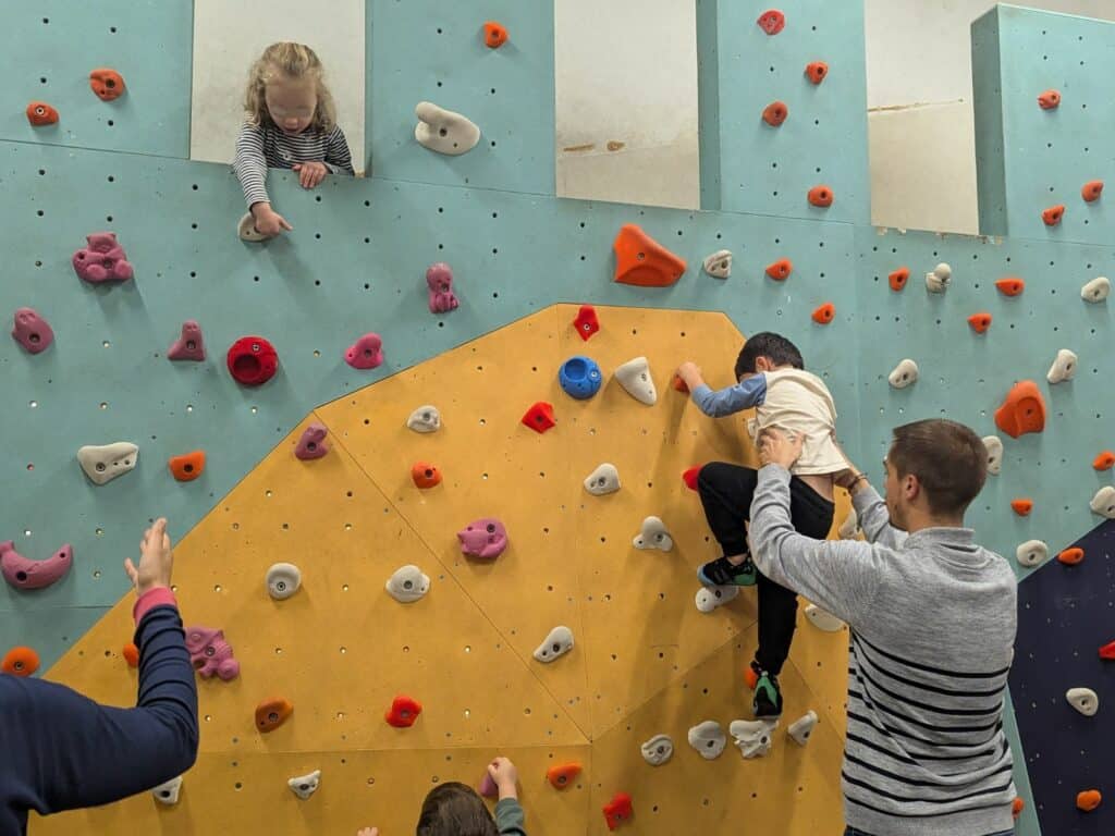 Enfant grimpant sur un mur d'escalade, soutenu par un psychomotricien